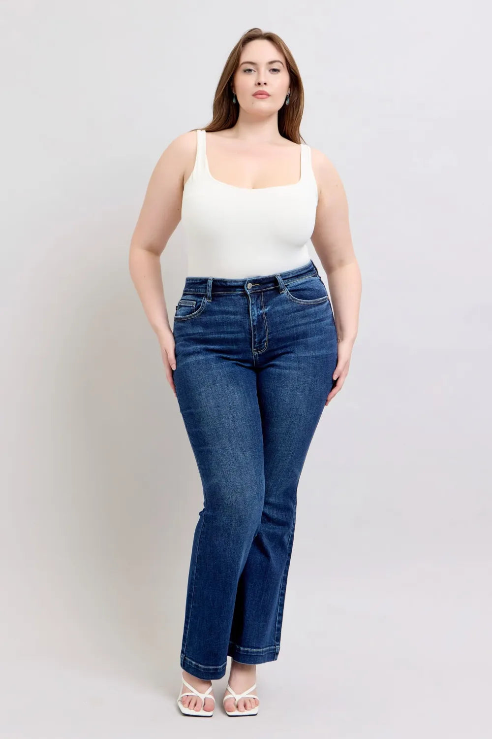 Woman wearing a white tank top and blue jeans against a plain background