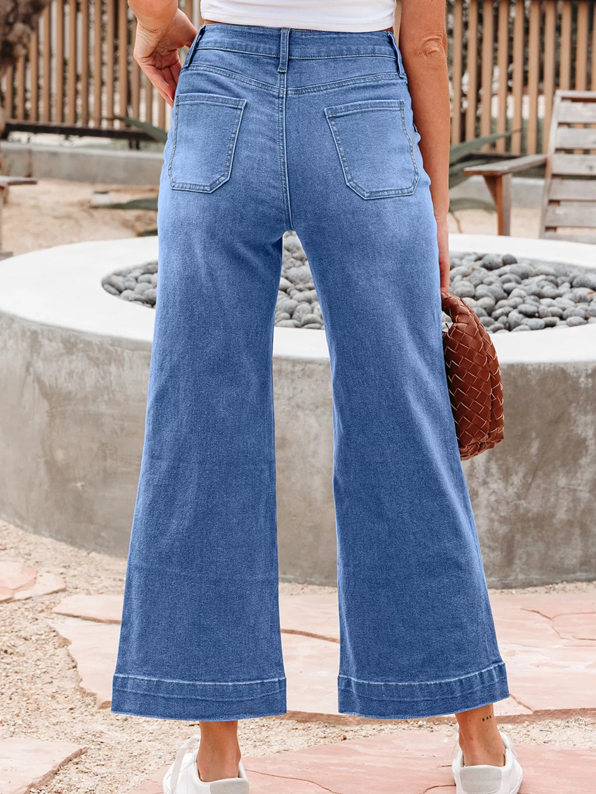 Person wearing blue wide-leg jeans standing outdoors near a stone wall.