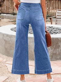 Person wearing blue wide-leg jeans standing outdoors near a stone wall.