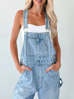 Person wearing light blue denim overalls on a plain background