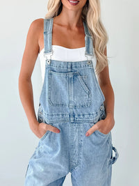 Person wearing light blue denim overalls on a plain background