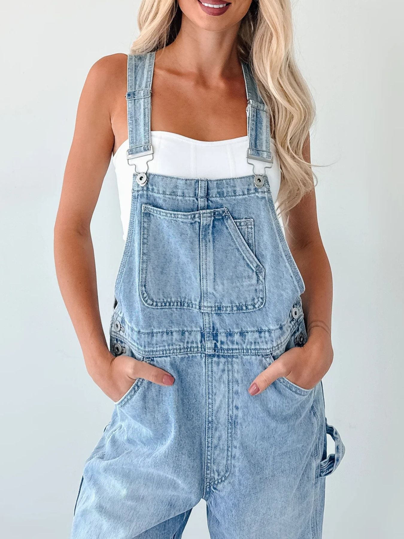 Person wearing light blue denim overalls on a plain background