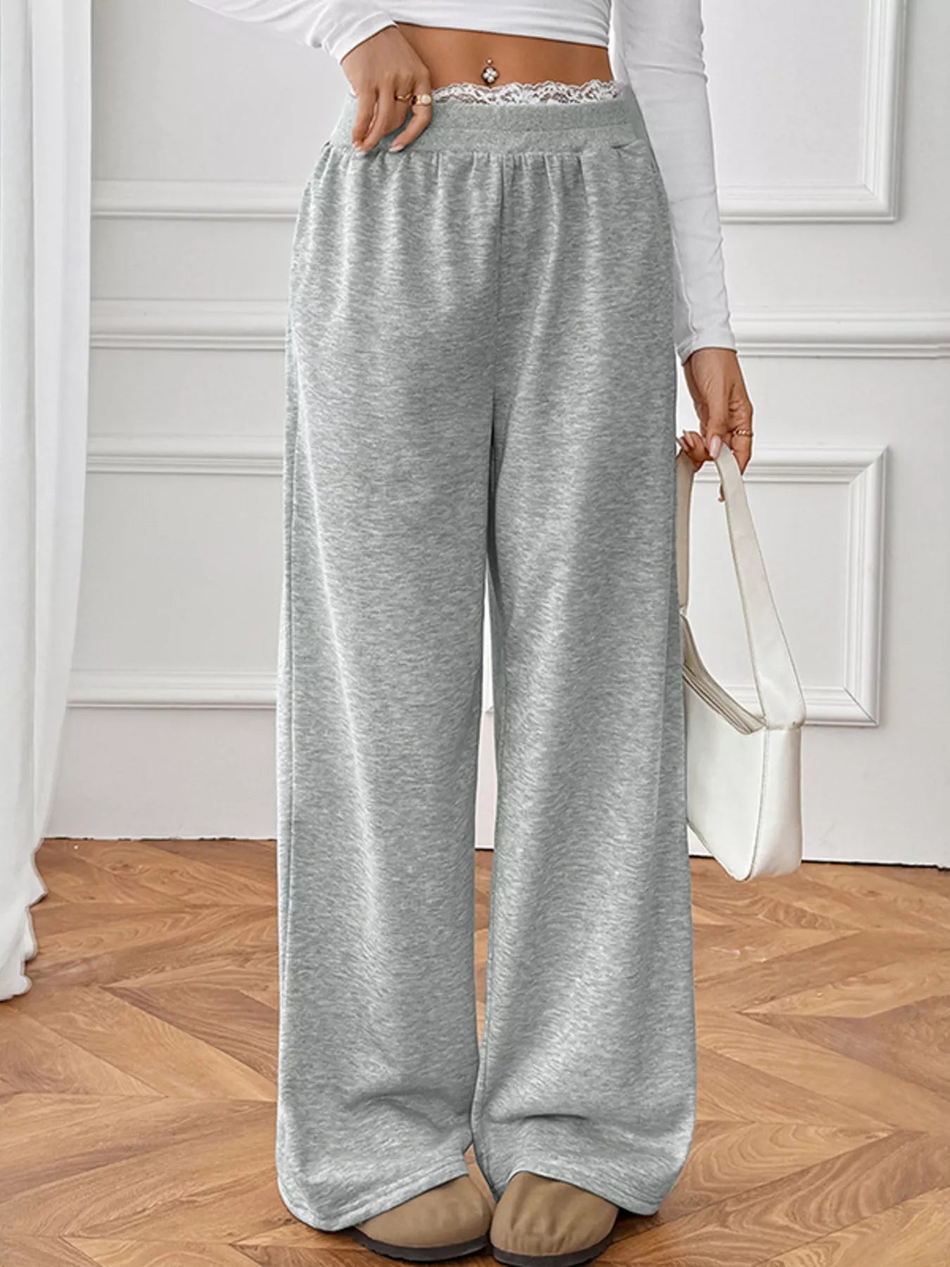 Person wearing gray wide-leg pants with a white top in a minimal indoor setting.
