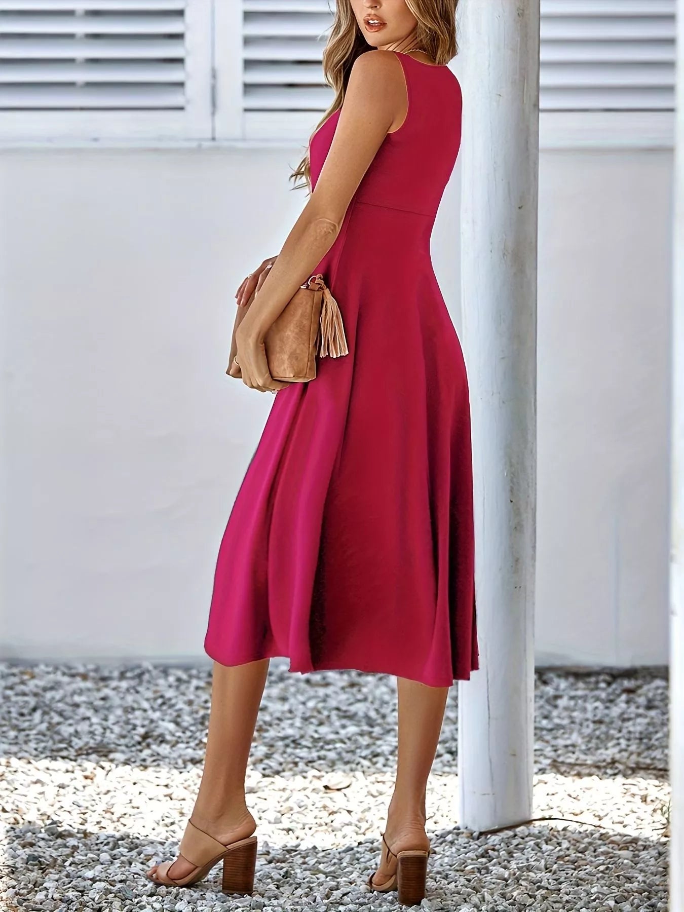 Woman wearing a red dress holding a beige clutch against a white background