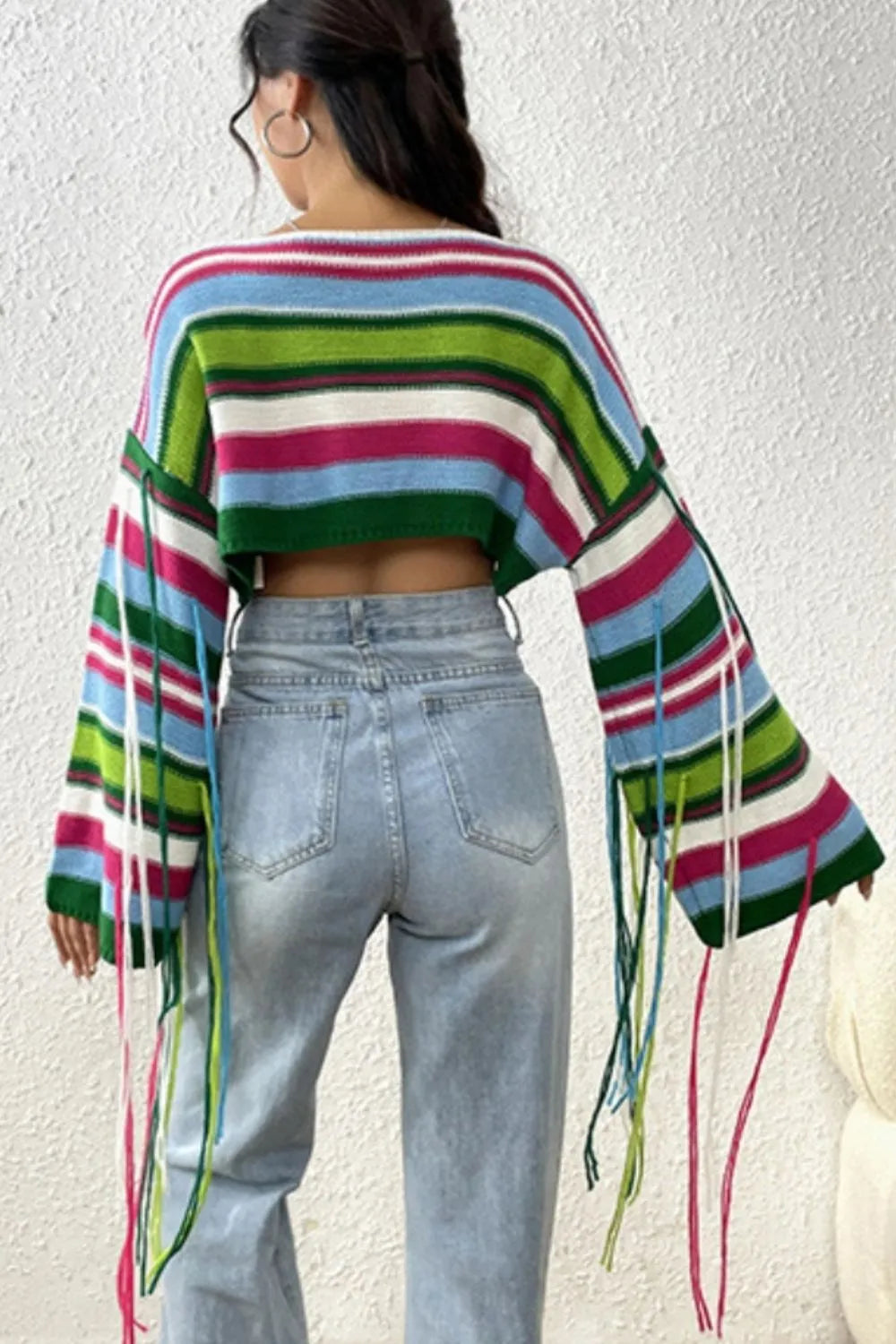 Person wearing a colorful striped sweater and light blue jeans against a white wall.