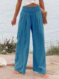 Person wearing blue wide-leg pants standing on a sandy beach with a white wall in the background.
