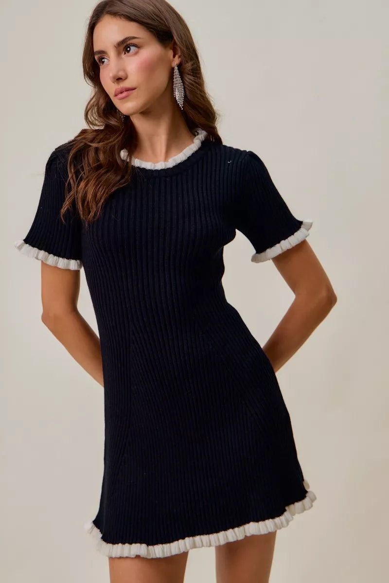 Woman wearing a black ribbed dress with white trim on a plain background