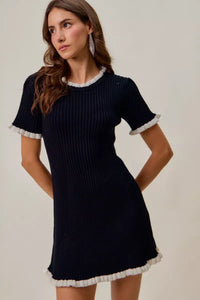 Woman wearing a black ribbed dress with white trim on a plain background