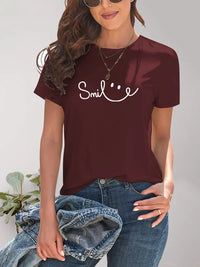 Woman wearing a maroon t-shirt with 'Smile' text design, standing against a neutral background.
