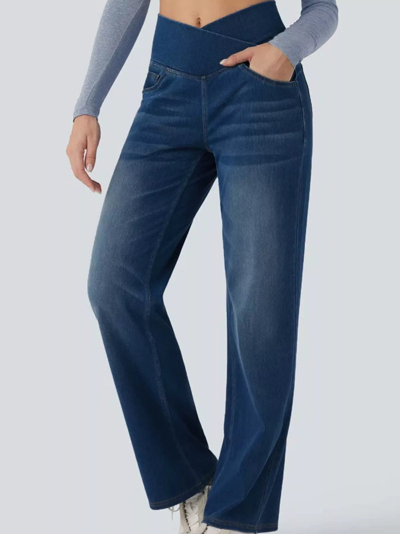 A person wearing dark blue high-waisted wide-leg jeans with a side pocket, paired with a gray long-sleeve top, shown from the waist down against a light gray background.