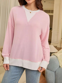 Person wearing a pink ribbed sweater over a white shirt with blue jeans indoors.