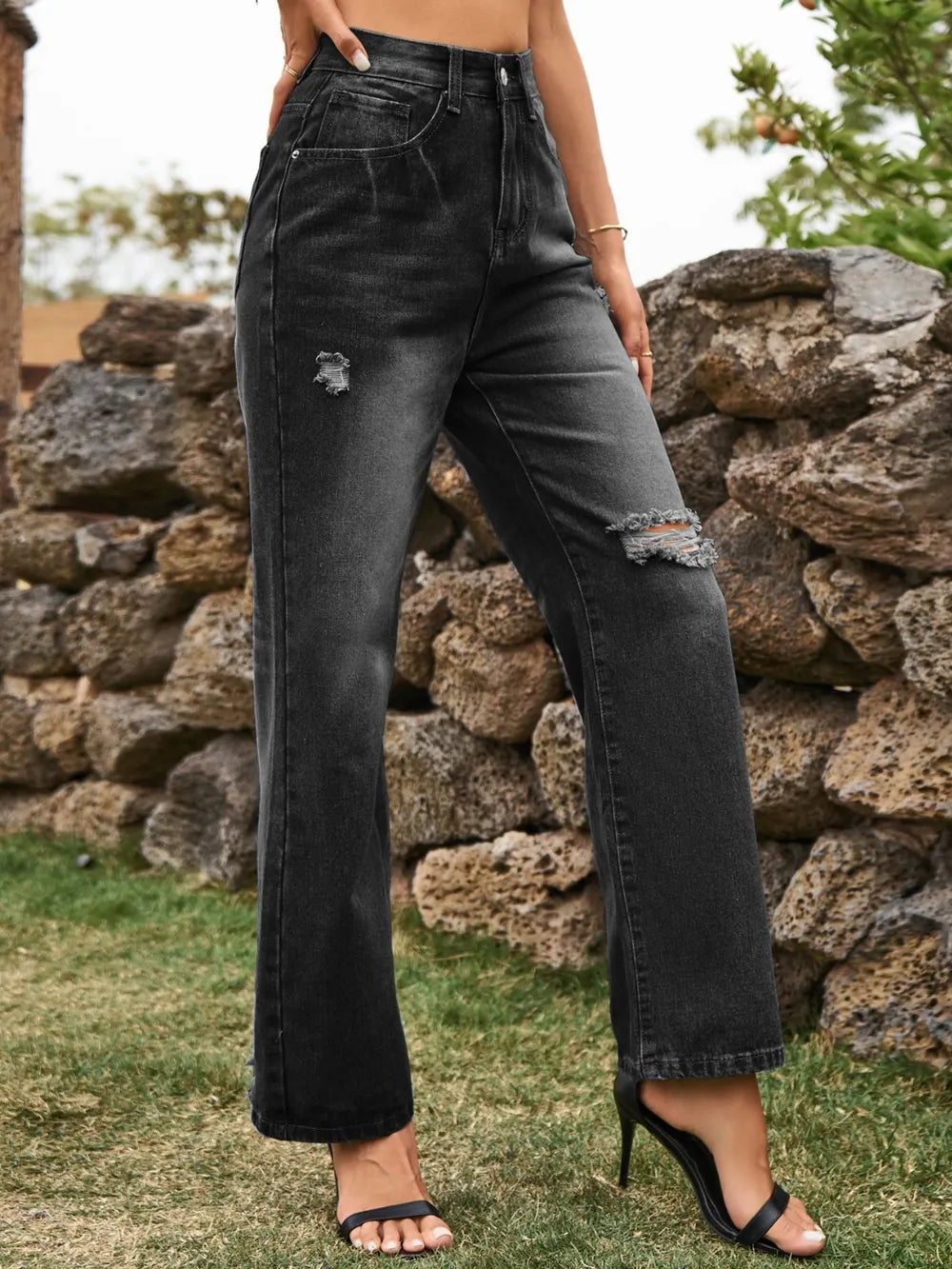 Person wearing black distressed jeans standing in front of a stone wall.