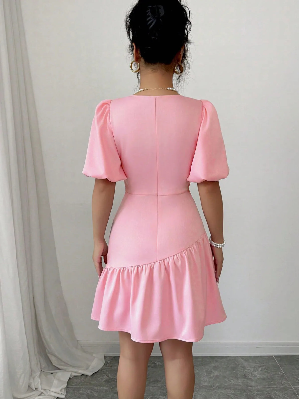 Person wearing a pink dress with puff sleeves against a white wall.