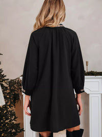 Person wearing a black dress standing in a room with a Christmas tree and fireplace.