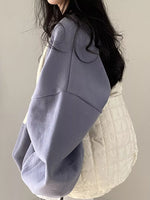 A person wearing an oversized lavender-gray pullover top layered over a cream quilted puffer jacket, shown from the side against a plain light background.