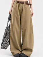 A person wearing high-waisted, wide-leg khaki pants with a brown belt, holding a black and white gingham tote bag against a plain light gray studio background.