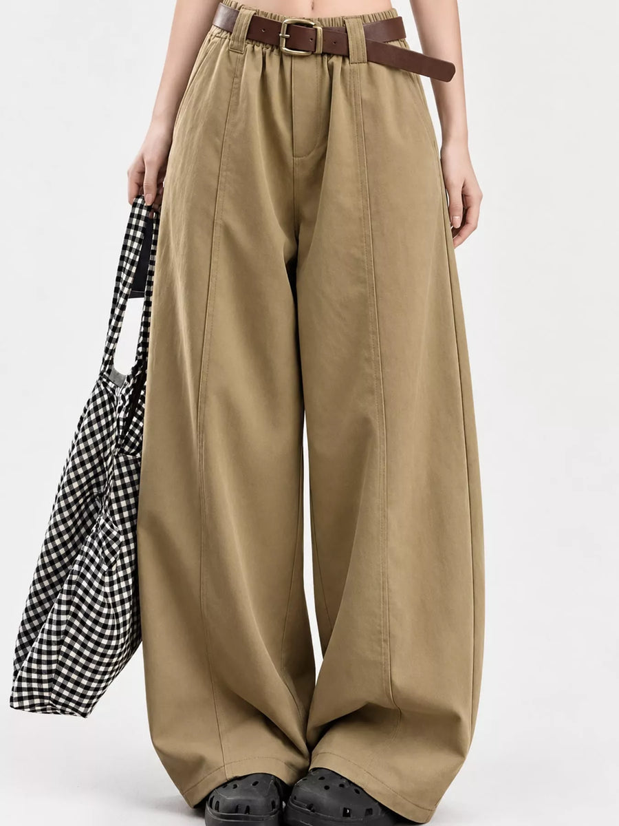 A person wearing high-waisted, wide-leg khaki pants with a brown belt, holding a black and white gingham tote bag against a plain light gray studio background.
