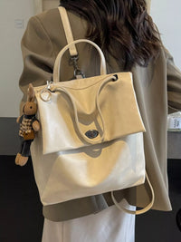 Beige handbag with a small plush toy attached, worn by a person in a beige coat.