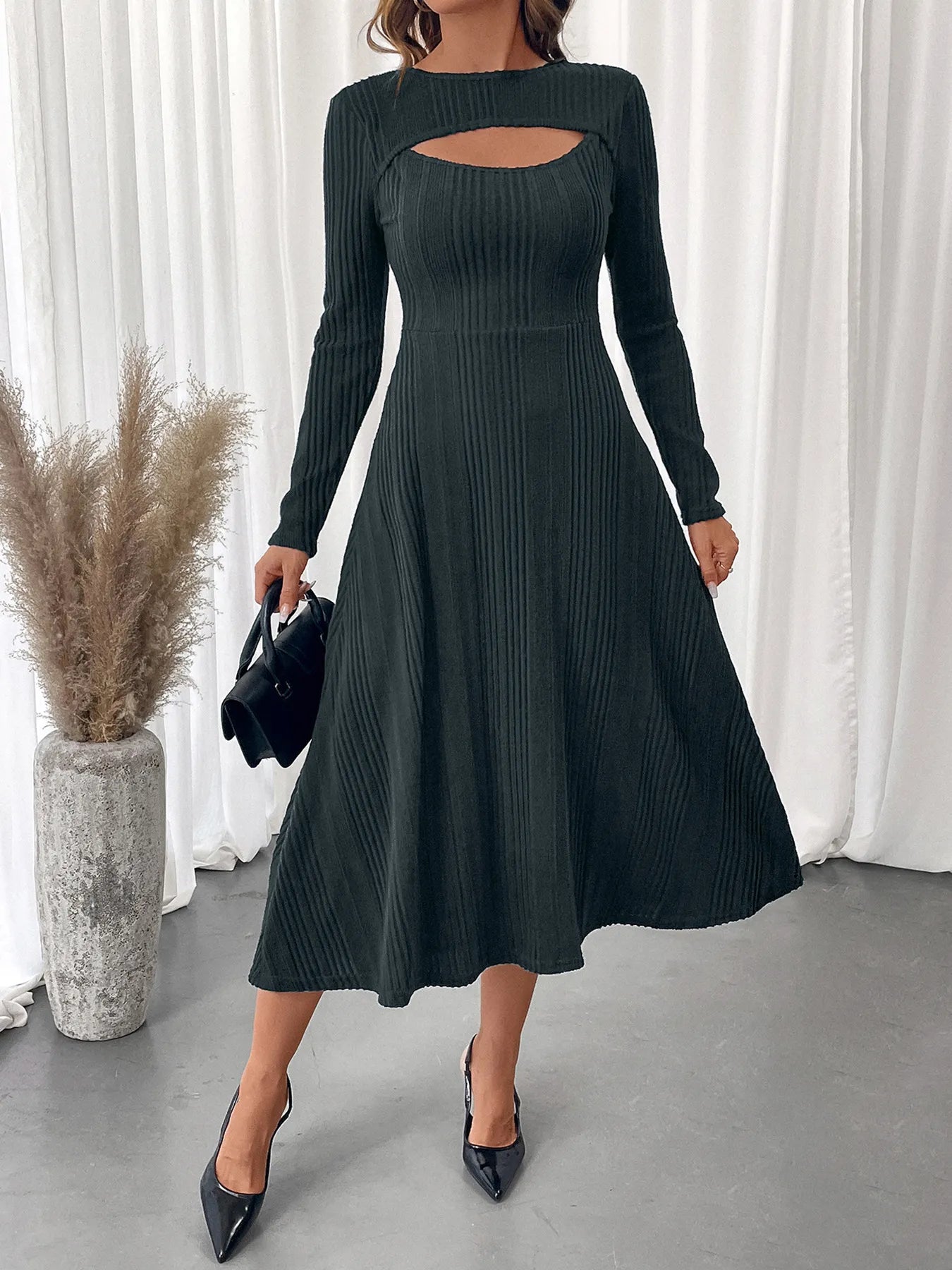 Woman wearing a black ribbed dress with cut-out design in a minimalistic setting.