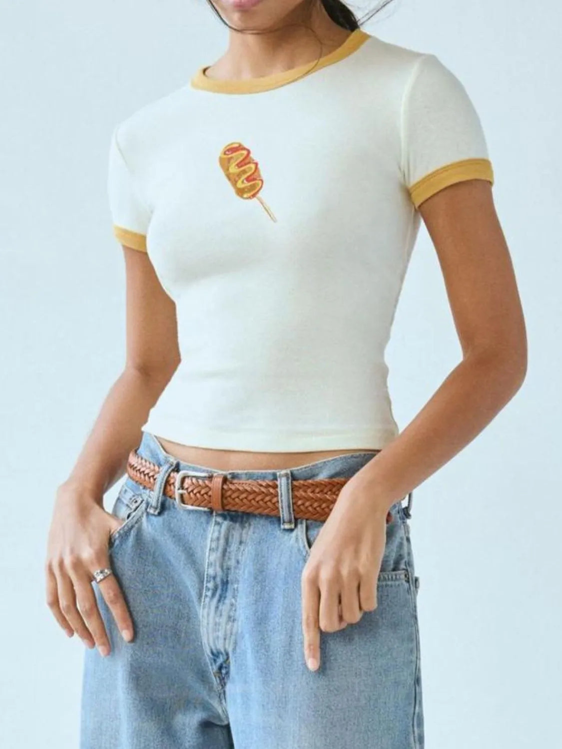 Person wearing a white crop top with yellow trim and blue jeans on a light gray background