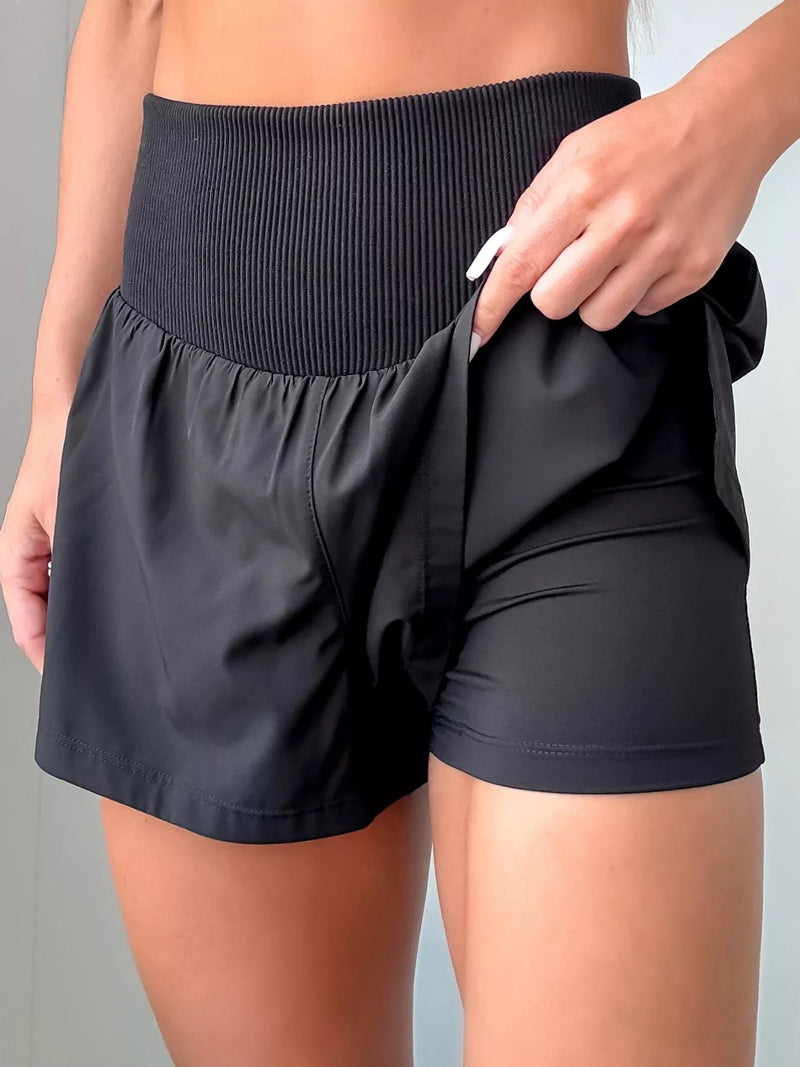 Black athletic shorts being adjusted by a person against a neutral background