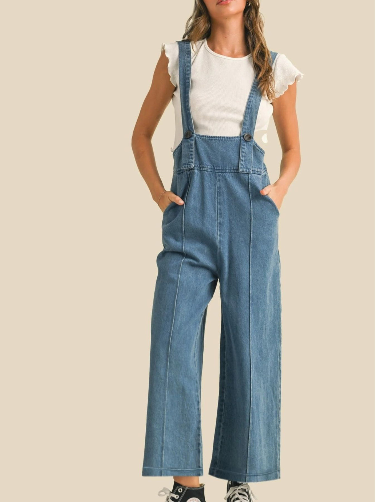 Person wearing blue denim overalls on a beige background