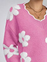 Pink sweater with white floral patterns on a plain background
