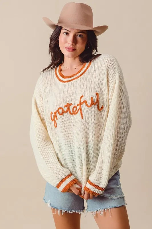 Woman wearing a cream sweater with 'grateful' text and a beige hat on a beige background