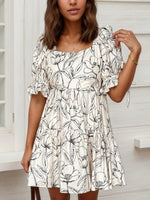 Woman wearing a white dress with black floral pattern indoors.