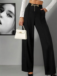Person wearing black high-waisted pants with a white handbag against a gray background