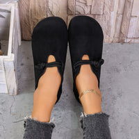 Black slippers worn by a person on a concrete floor with a stone wall background