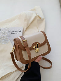 Small beige and brown handbag held by a hand on a light background