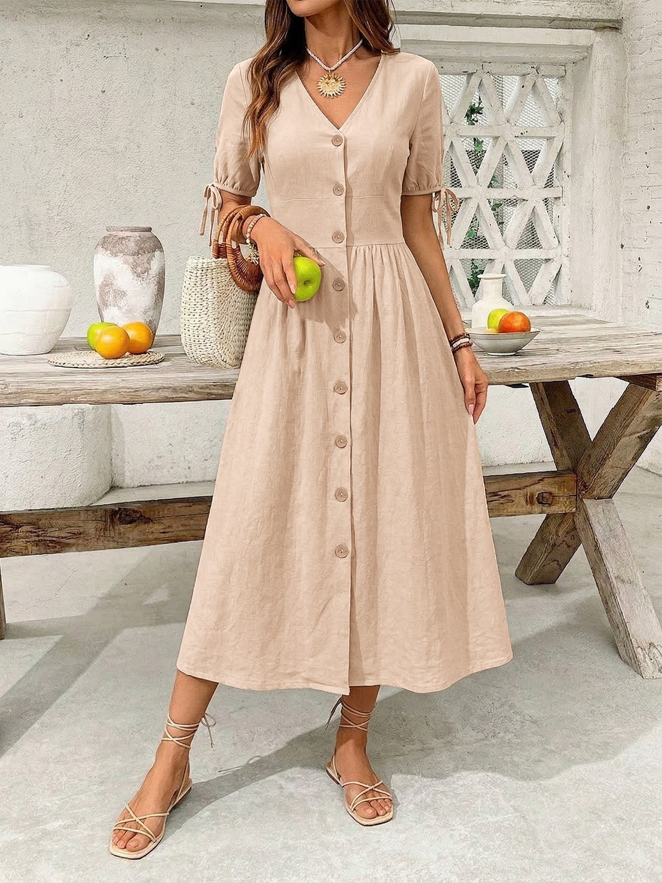 Woman in a beige dress holding an apple in a casual setting.