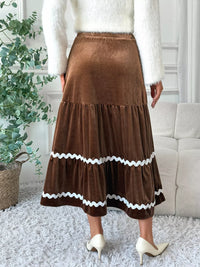 Person wearing a brown tiered skirt with white trim in a home setting.