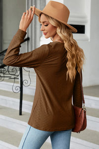 Woman wearing a brown sweater and hat, holding a brown handbag indoors.