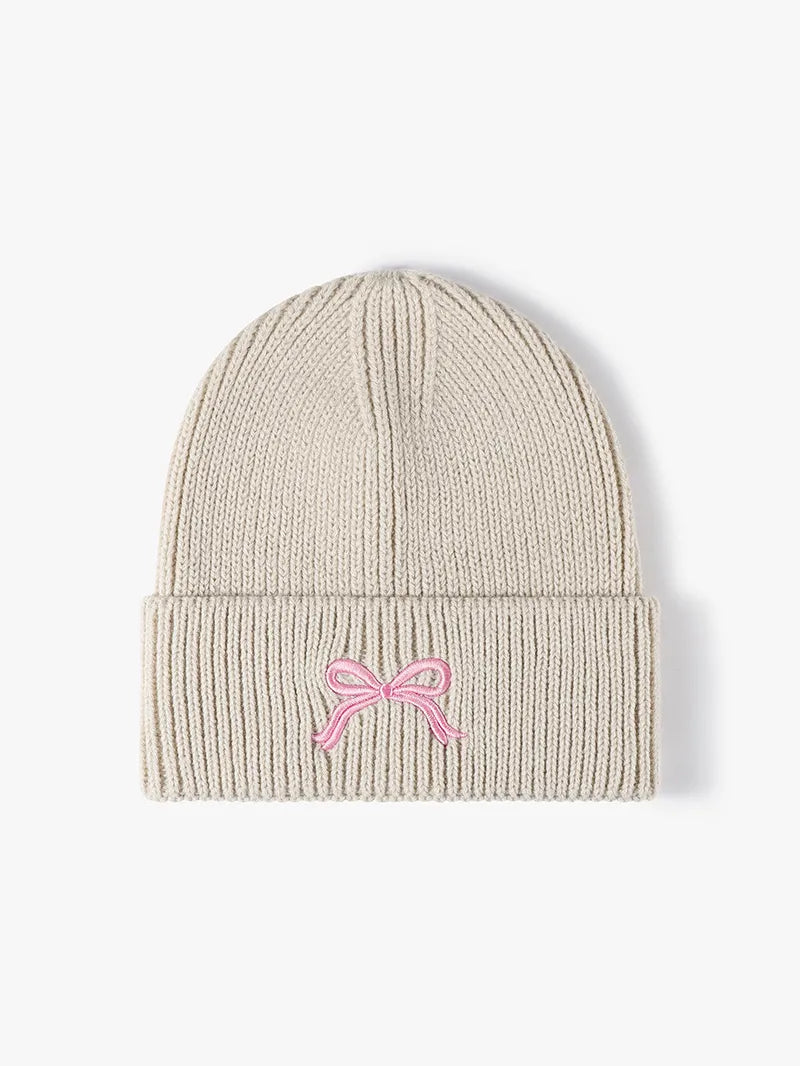 Beige knit beanie with a pink bow on a white background