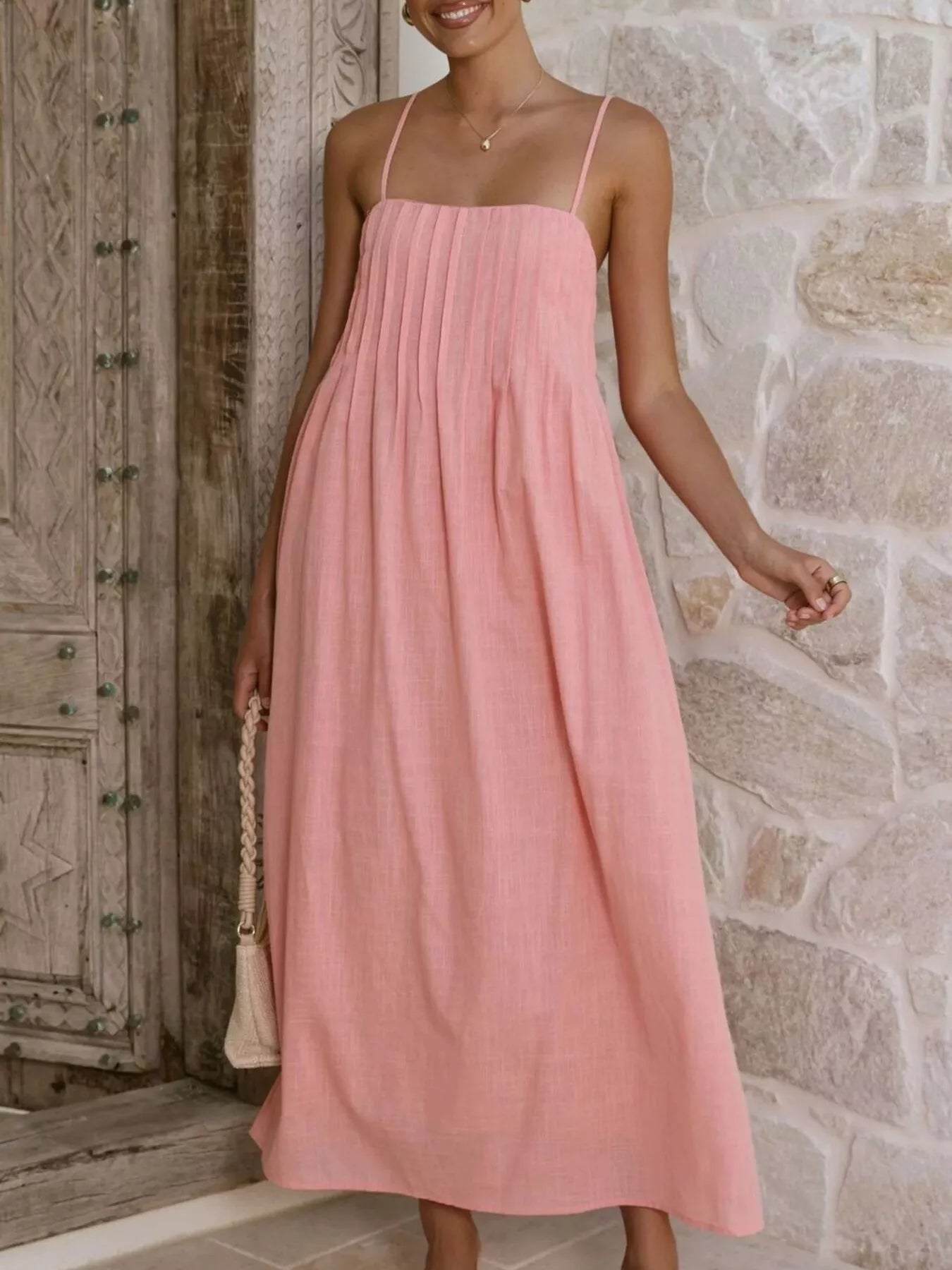 Woman wearing a pink dress standing against a stone wall.