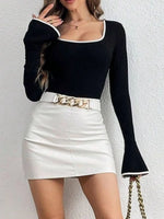 Person wearing a black long-sleeve top and white skirt with a gold belt against a white background