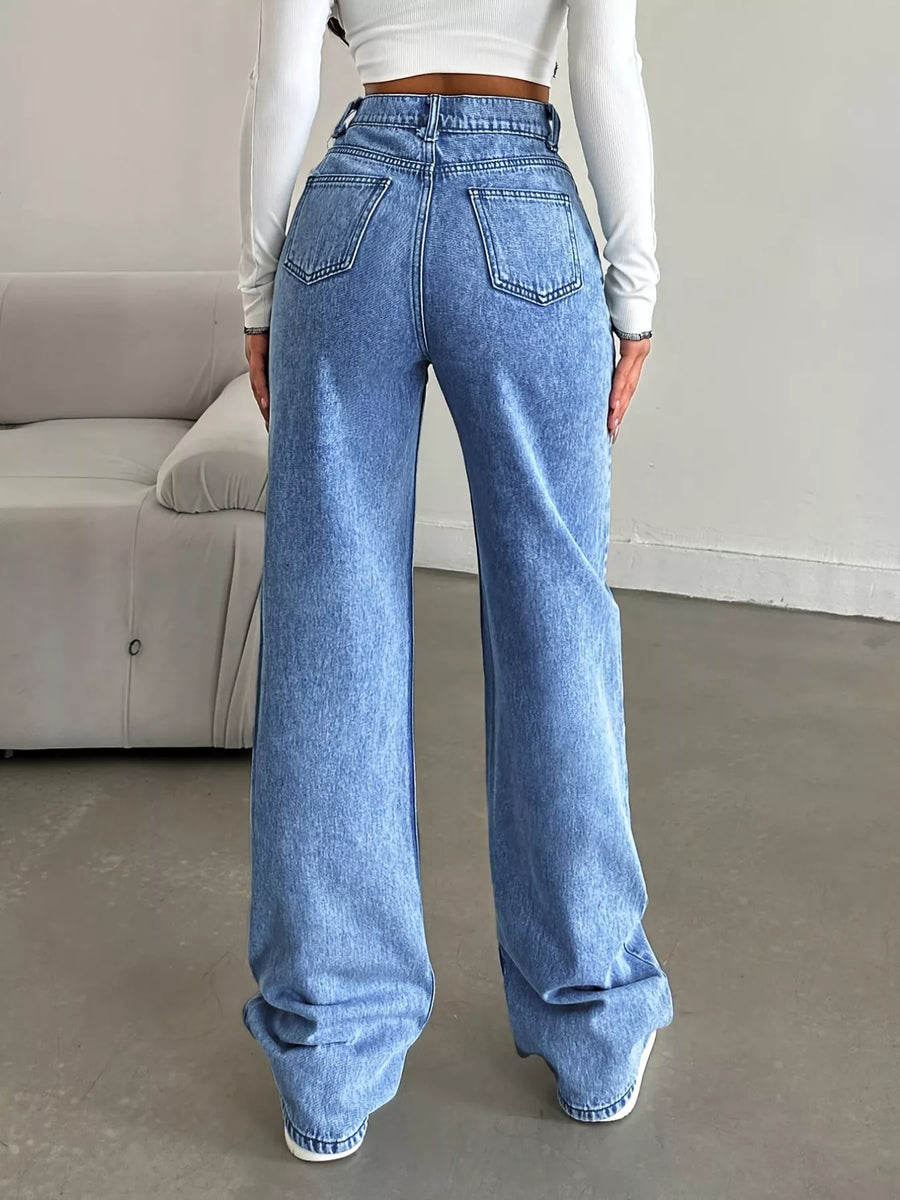 Person wearing blue jeans and a white long-sleeve top in a minimal indoor setting.