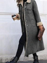 Person wearing a long gray coat with fur trim, holding a coffee cup and clutch.
