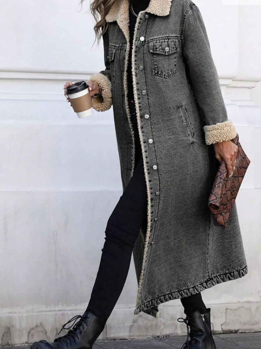 Person wearing a long gray coat with fur trim, holding a coffee cup and clutch.