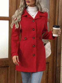 Person wearing a red coat holding a coffee cup in front of a wooden door.