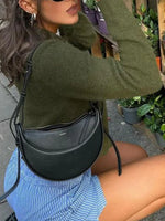 Person wearing a green sweater and blue shorts with a black handbag outdoors.