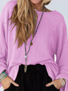 Person wearing a pink sweater and black pants with a long necklace.