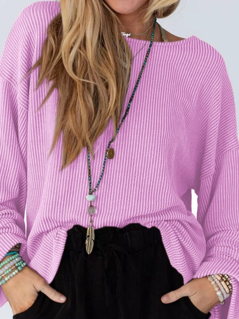Person wearing a pink sweater and black pants with a long necklace.