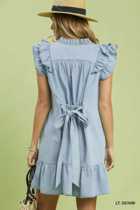 Woman wearing a light denim dress with ruffled details on a green background