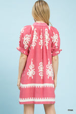 Woman wearing a pink dress with white embroidery on a light blue background