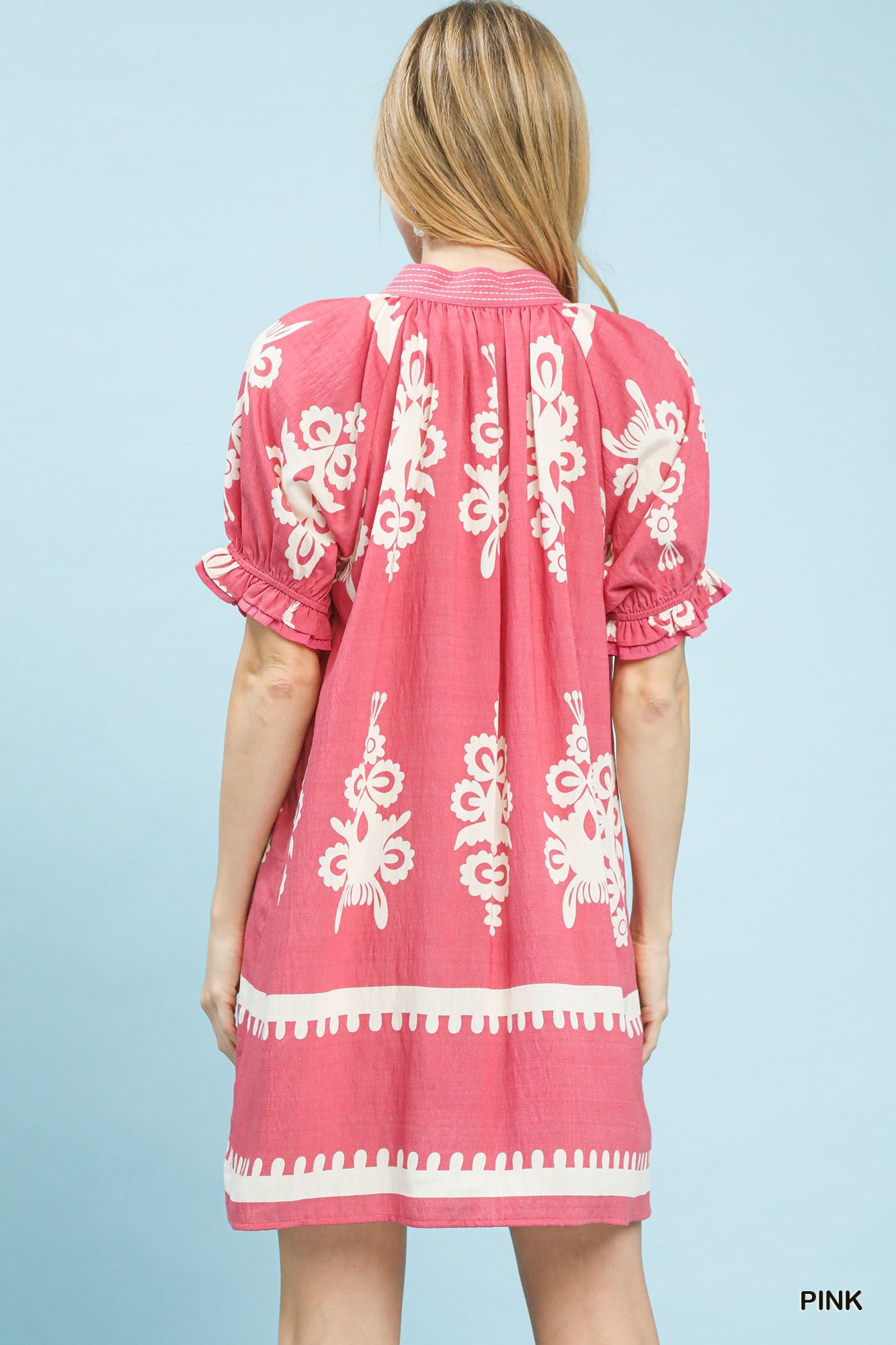 Woman wearing a pink dress with white embroidery on a light blue background