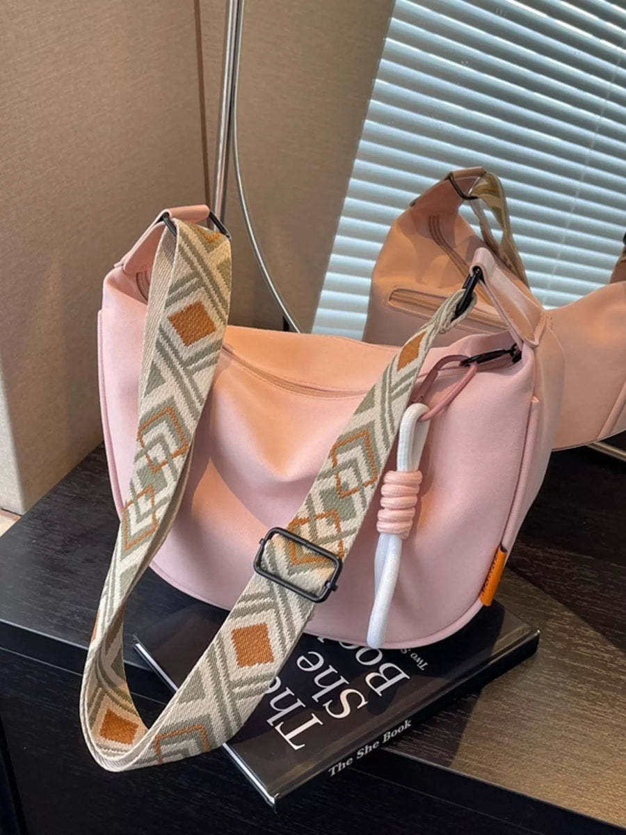Pink handbag with a patterned strap on a black surface