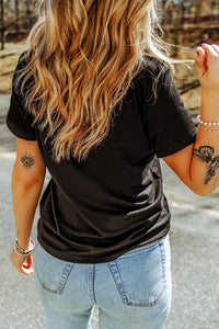 Person wearing a black t-shirt and light blue jeans with tattoos on arms outdoors.